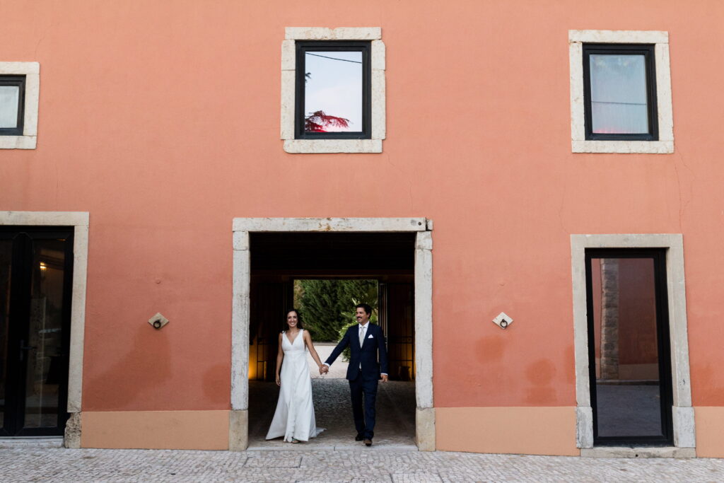 A relaxed and elegant destination wedding moment in Lisbon Couple walking hand in hand at a destination wedding in Lisbon framed by traditional Portuguese architecture