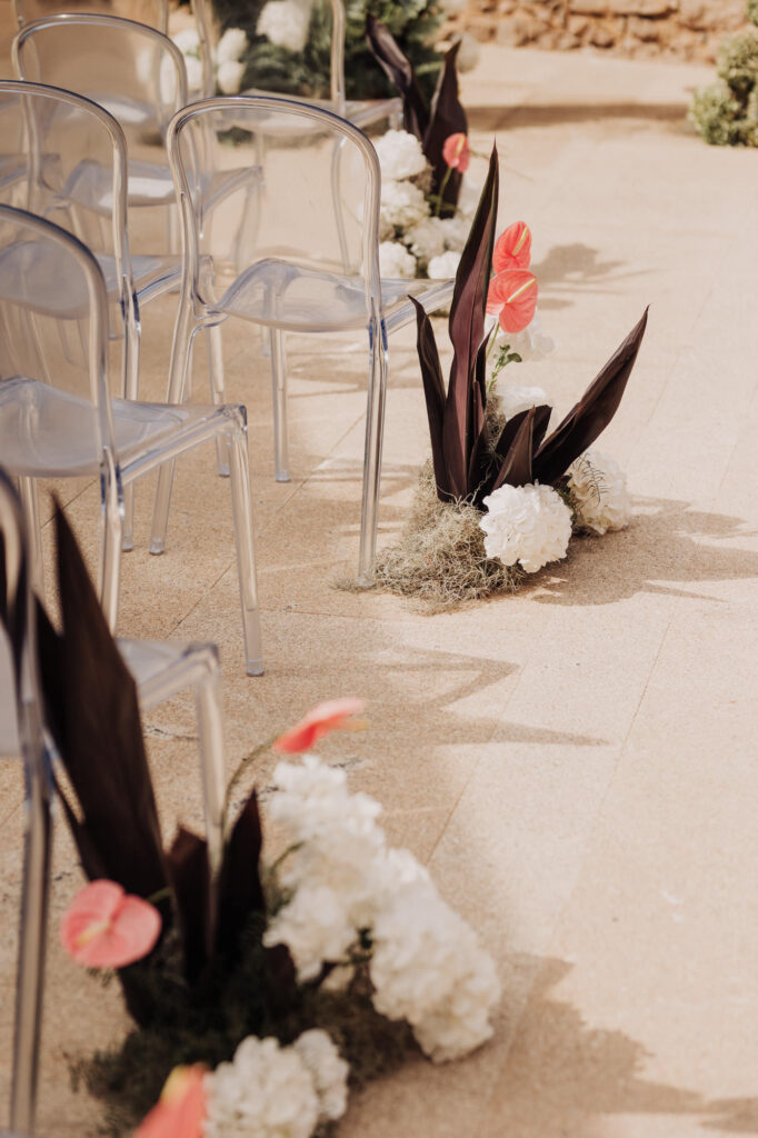 Intimate wedding ceremony setup in Cascais with transparent chairs and floral aisle arrangements by the sea