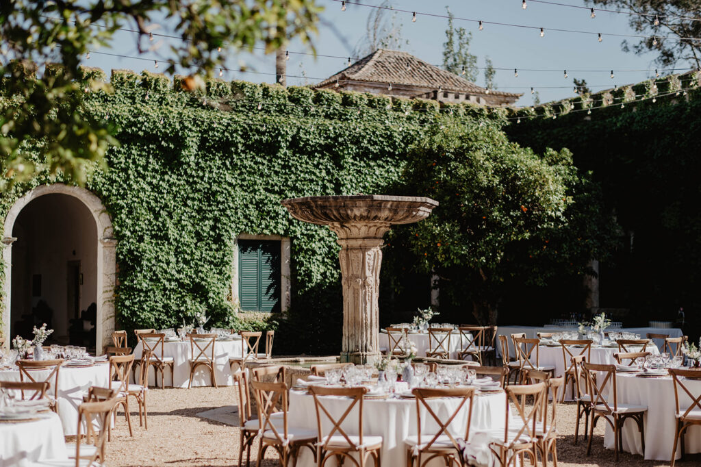 Outdoor wedding reception setup at a historic estate near Lisbon, Portugal, with elegant dining tables arranged in a garden courtyard surrounded by ivy-covered walls.