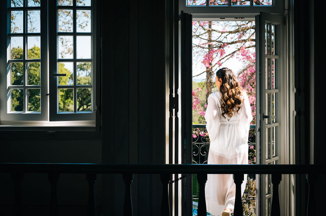 Bride in a white dress standing by an open balcony overlooking flowering trees