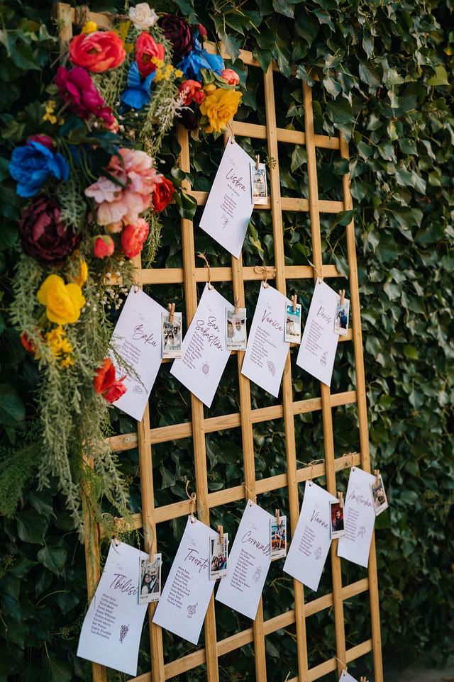Wedding seating plan cards hanging from a wooden trellis decorated with colourful flowers